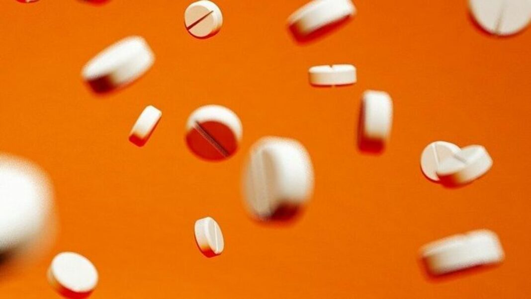 White pills falling on orange background.