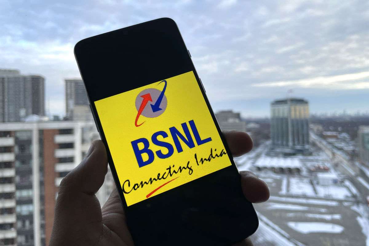 Hand holding phone with BSNL logo, city background.