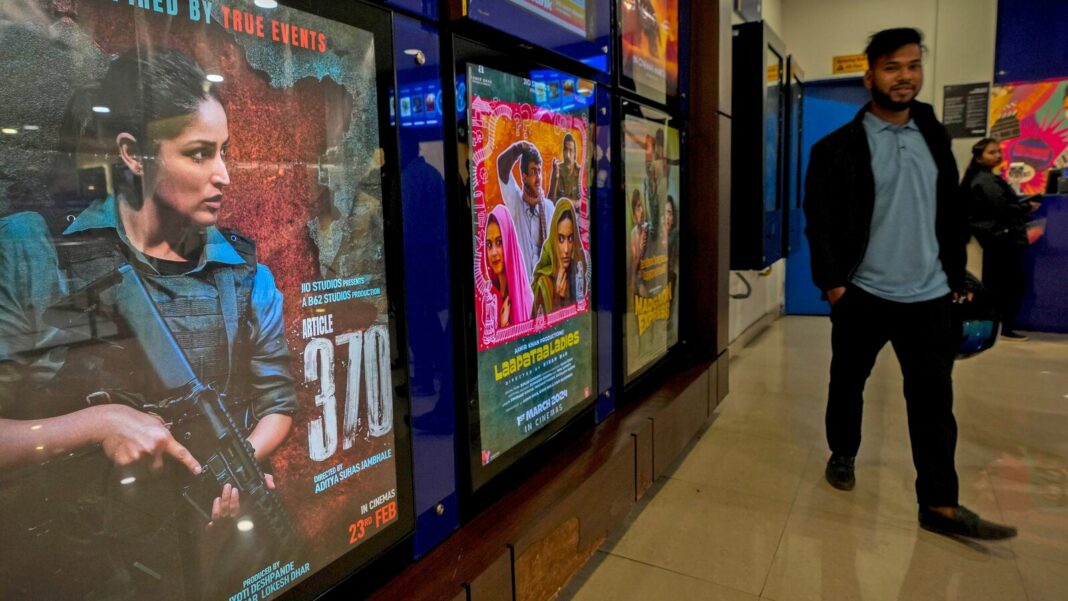 Man walking by movie posters in cinema lobby.