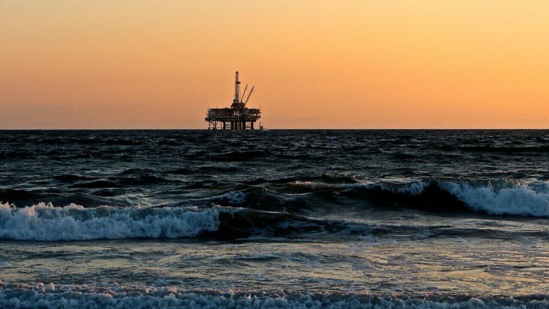Offshore oil rig at sunset with waves.