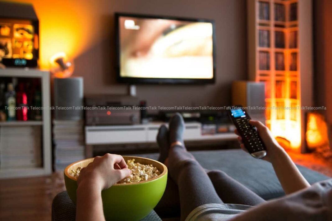 Person watching TV with popcorn and remote control.