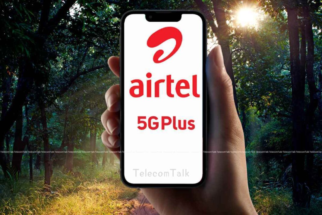 Hand holding smartphone with Airtel 5GPlus logo, forest background.