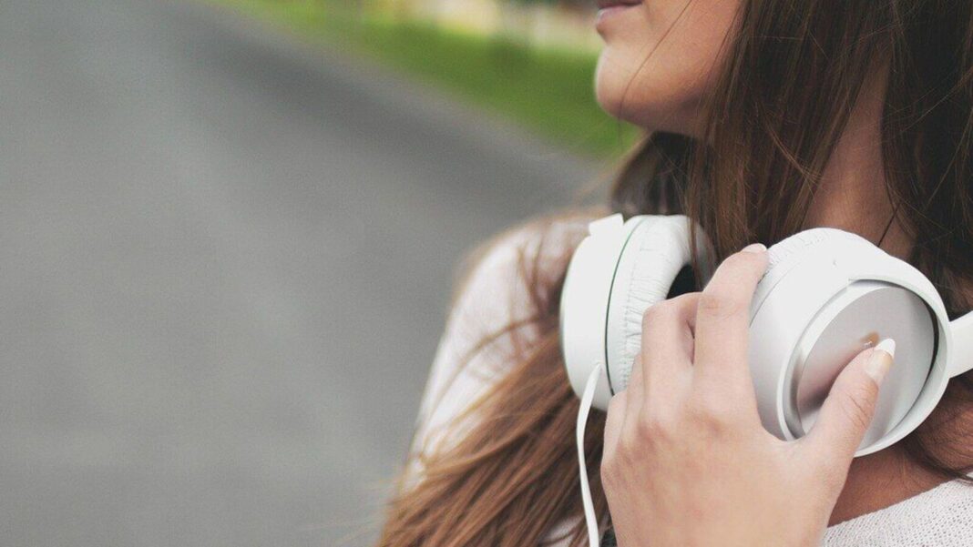Woman holding white headphones outdoors.