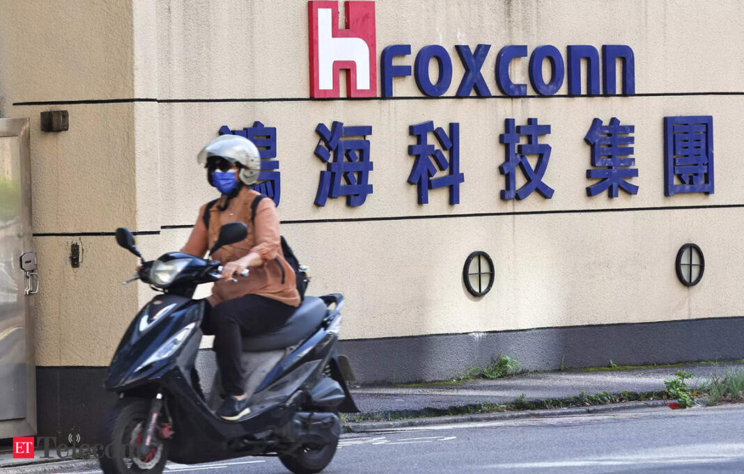 Person riding scooter past Foxconn building signage.