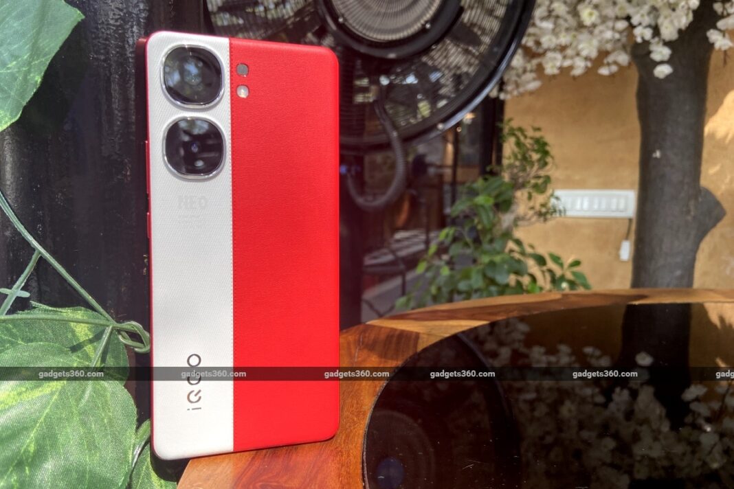 Red and white smartphone with dual cameras on wooden table.