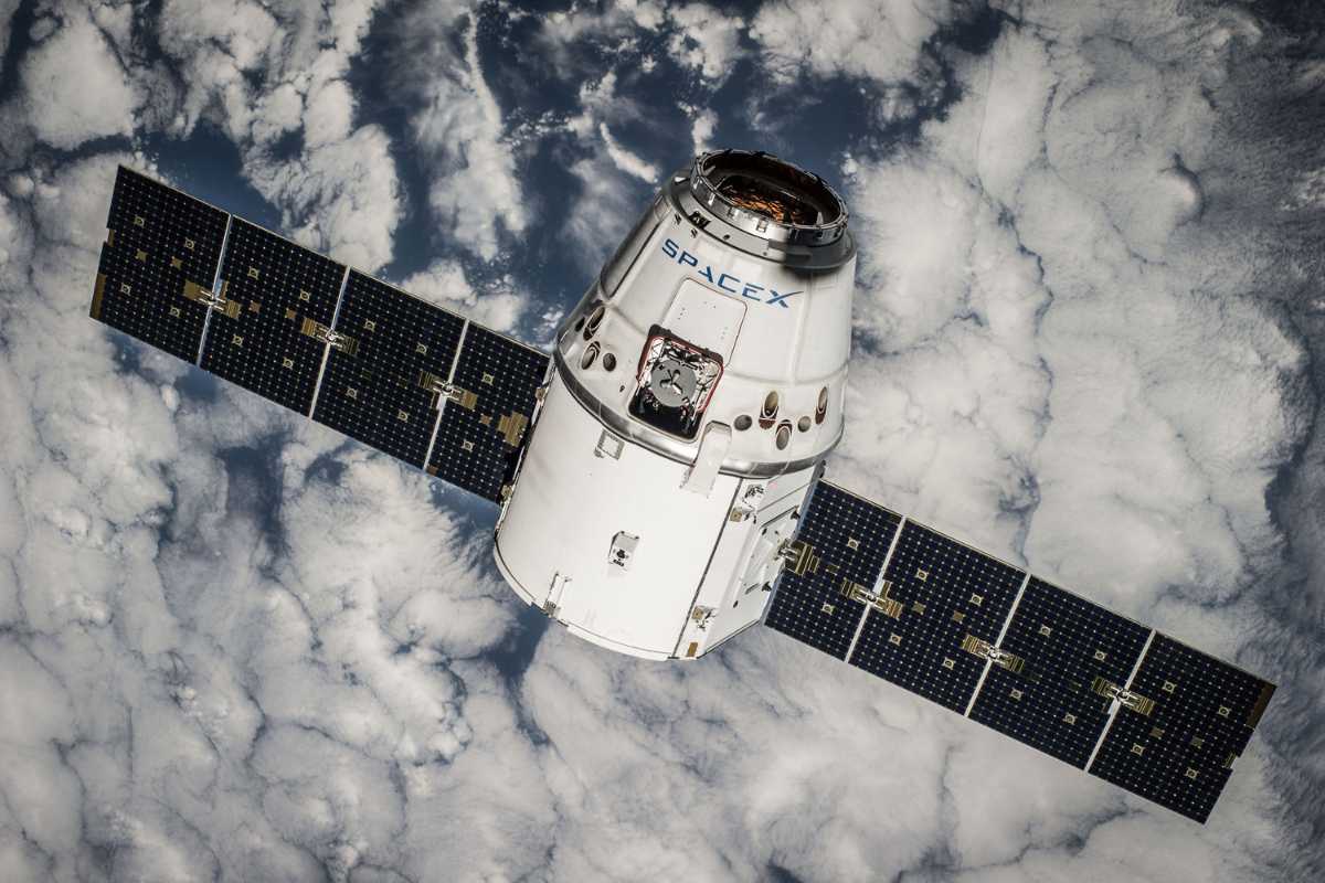 SpaceX spacecraft orbiting Earth over clouds.