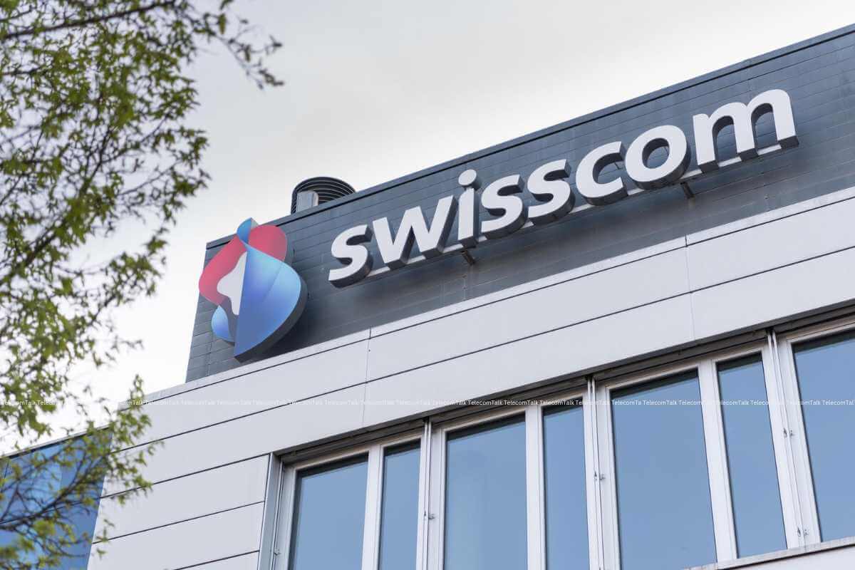 Swisscom logo on building exterior with tree branch.