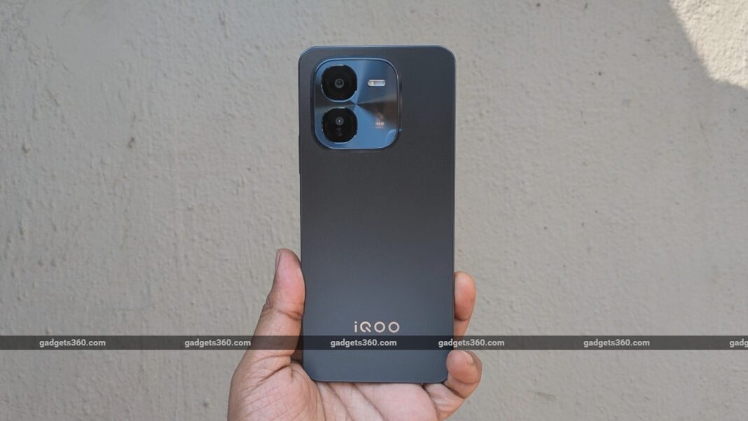Hand holding iQOO smartphone with dual camera.