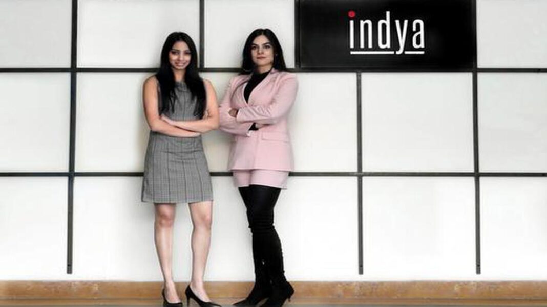 Two women posing by a company logo indoors.