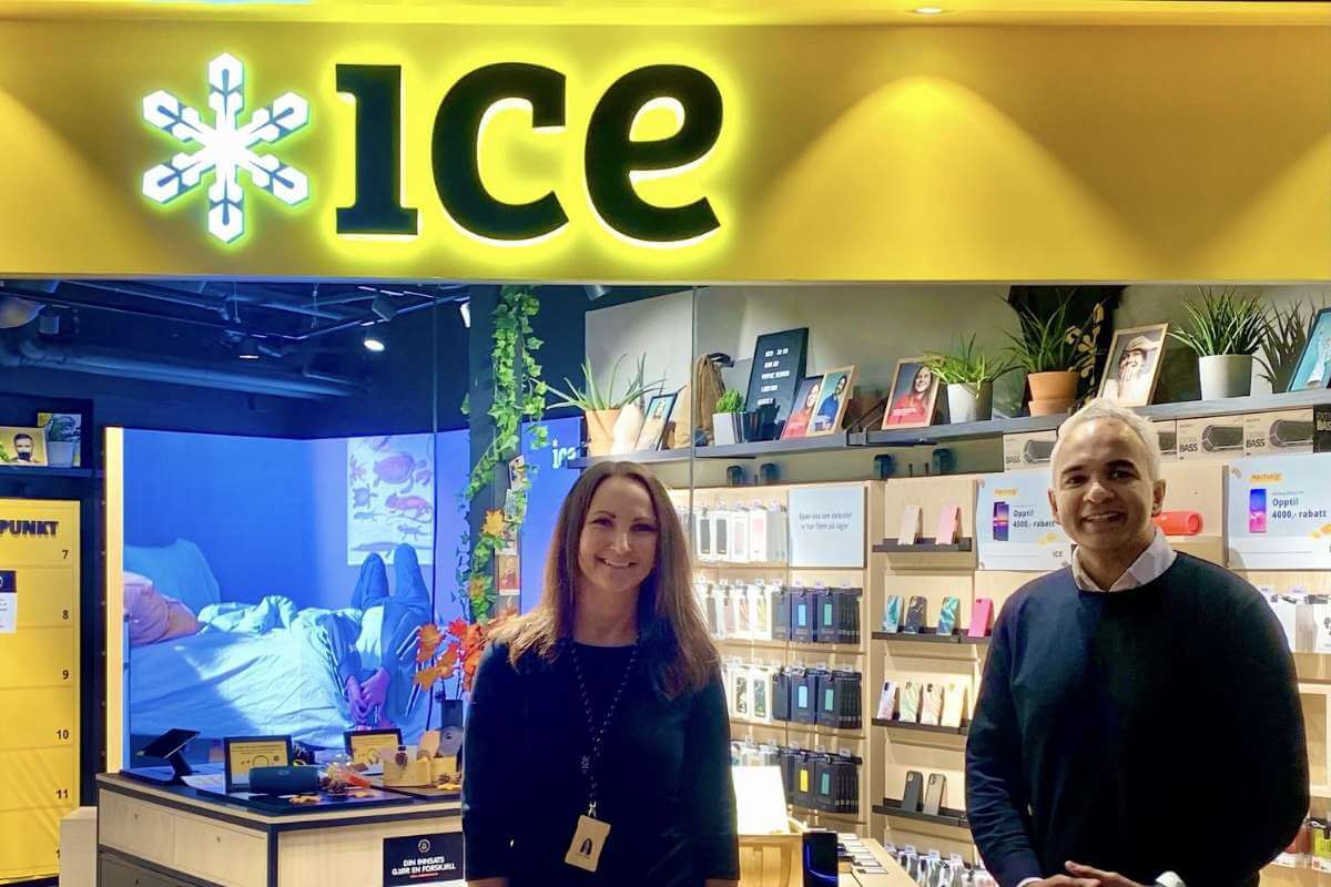 Two smiling employees in "Ice" store with electronics displays.