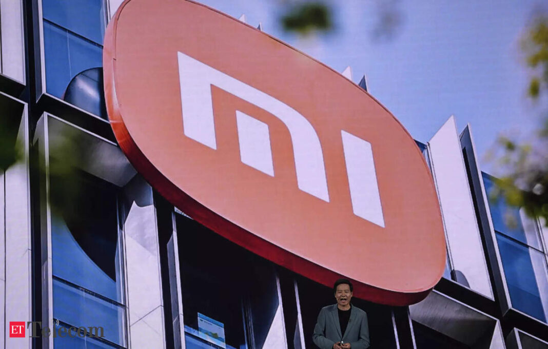 Xiaomi logo on building facade with person standing below.