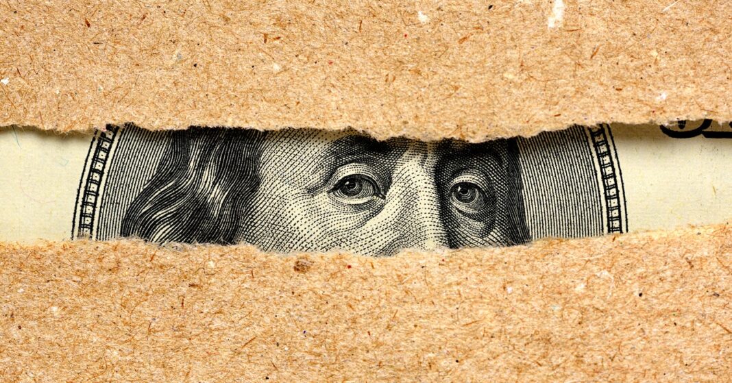 Dollar bill peeking through torn paper texture.