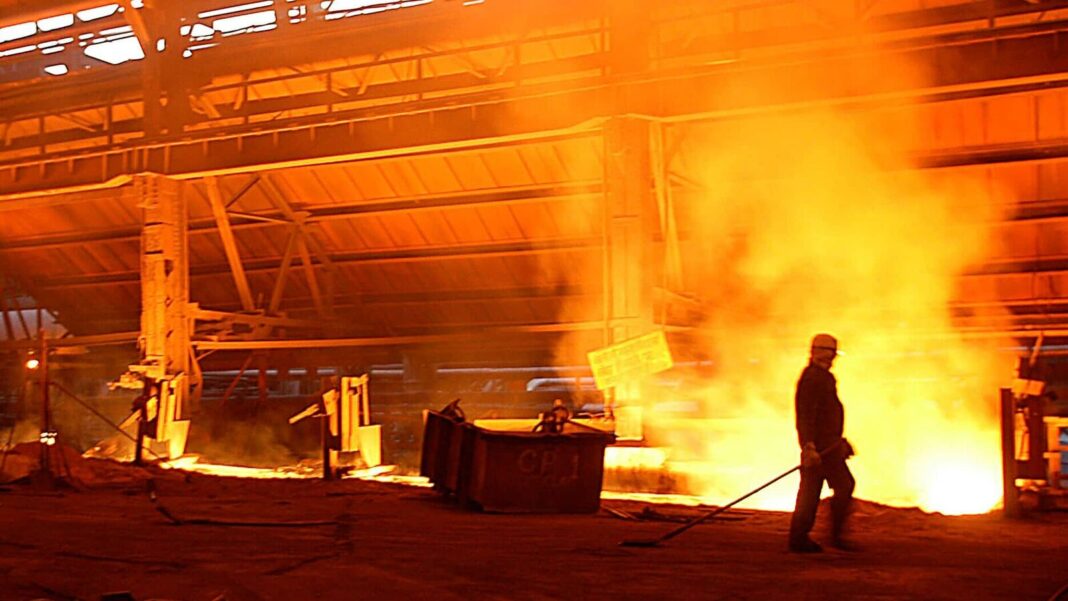 Worker near molten metal in steel mill.