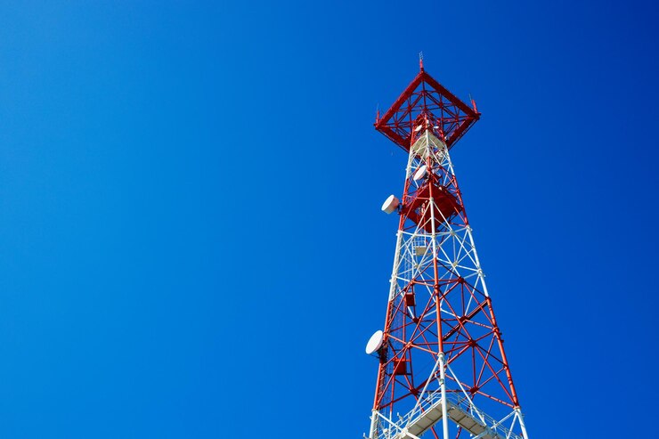 Red communication tower against clear blue sky.