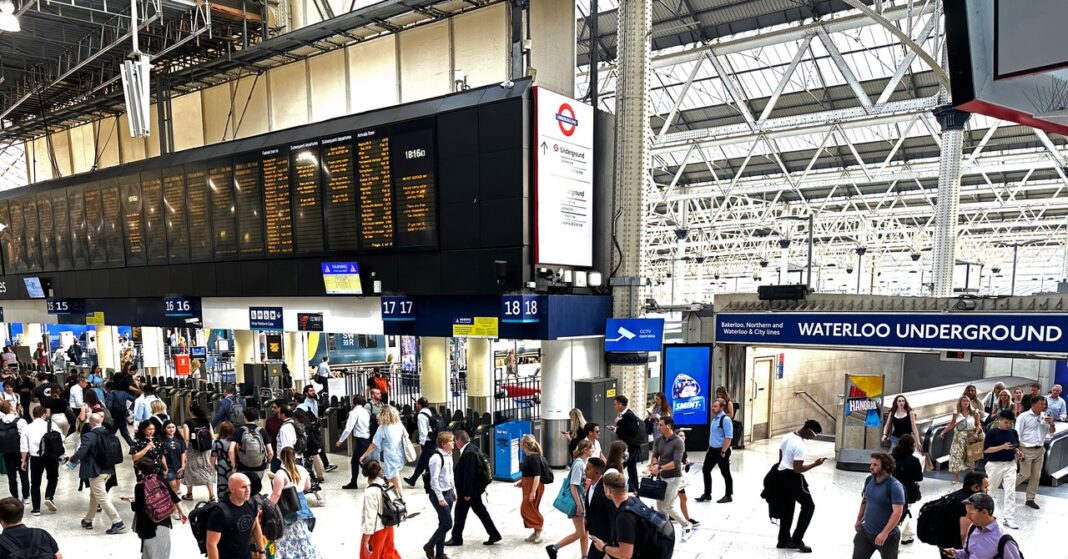 Busy train station with departure board and passengers.