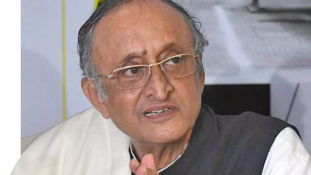 Elderly man speaking, wearing glasses and traditional attire.