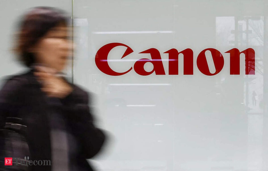 Canon logo on glass facade with blurred person passing by.