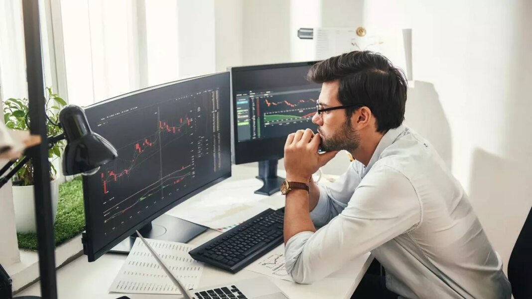 Man analyzing stock market data on dual monitors.