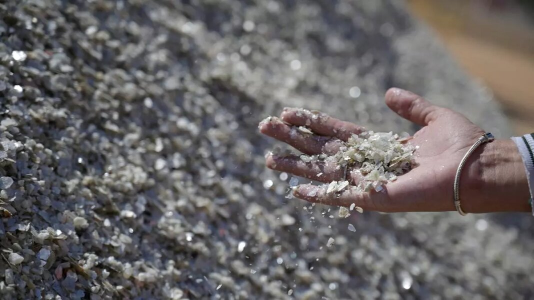 Hand sifting through crushed glass recycling materials.