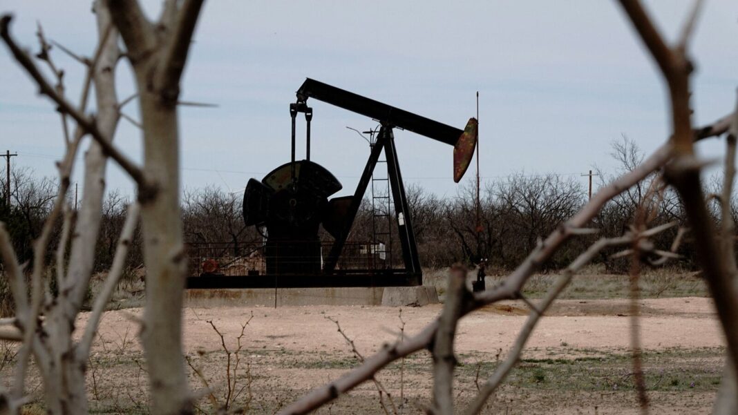 Oil pumpjack amidst trees in rural landscape.