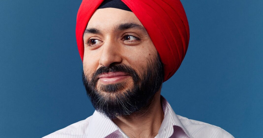 Man in red turban smiling against blue background.