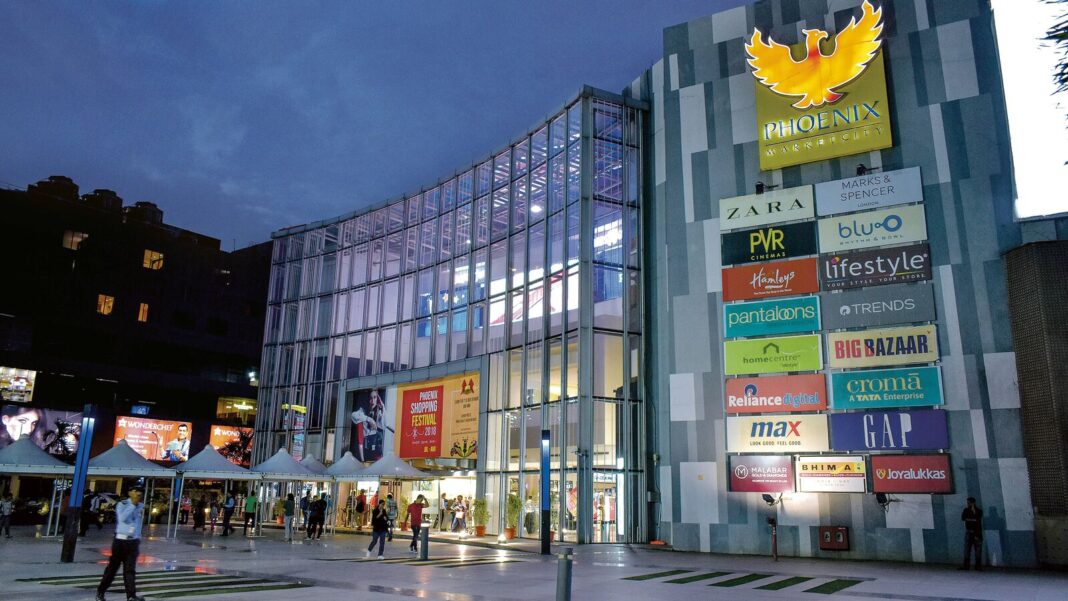Modern shopping mall facade with illuminated brand signs at dusk.