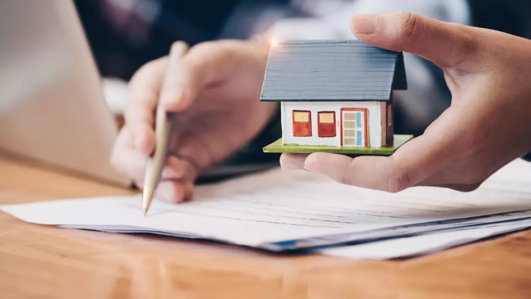 Person holding model house while signing document.