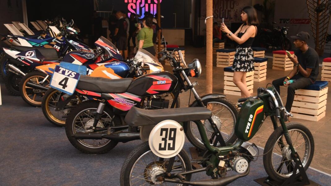 People examining racing motorcycles at an indoor event.