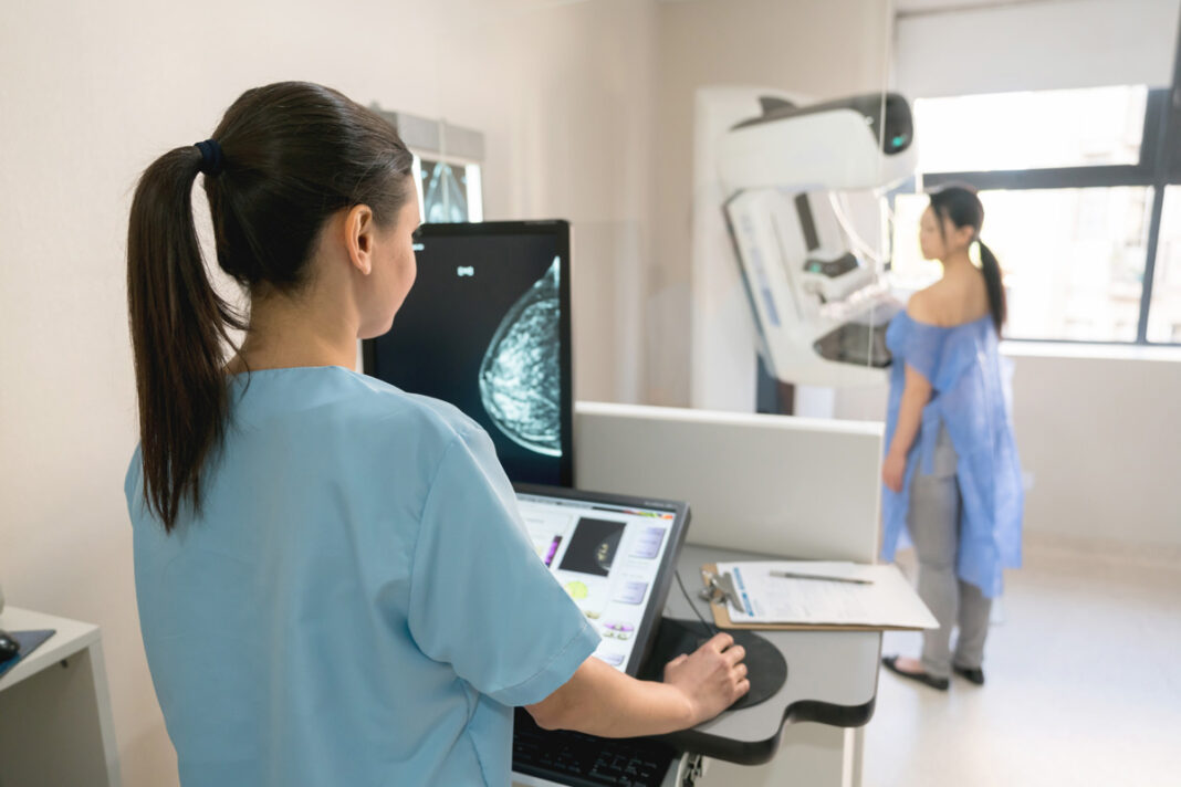 Technician operating mammogram machine with patient.