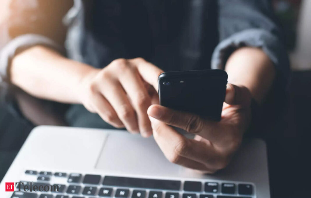 Person using smartphone above laptop keyboard.