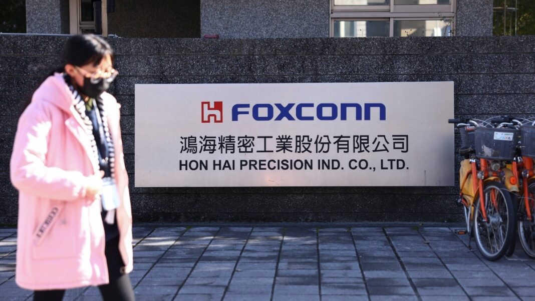 Person walking by Foxconn company sign outdoors.