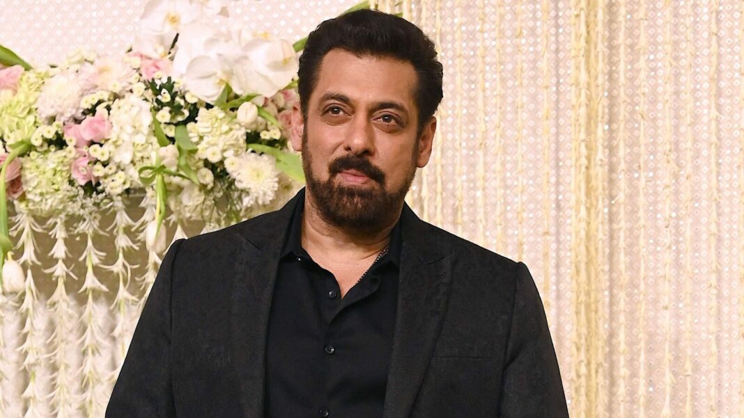 Man in black suit at event with floral background.