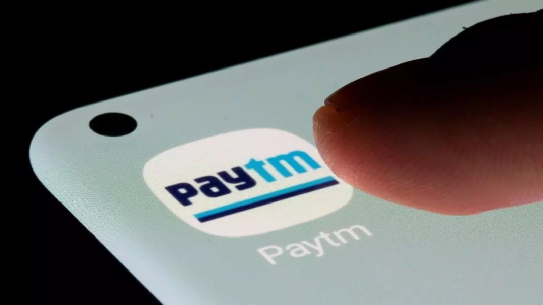 Finger tapping on Paytm app icon on phone.