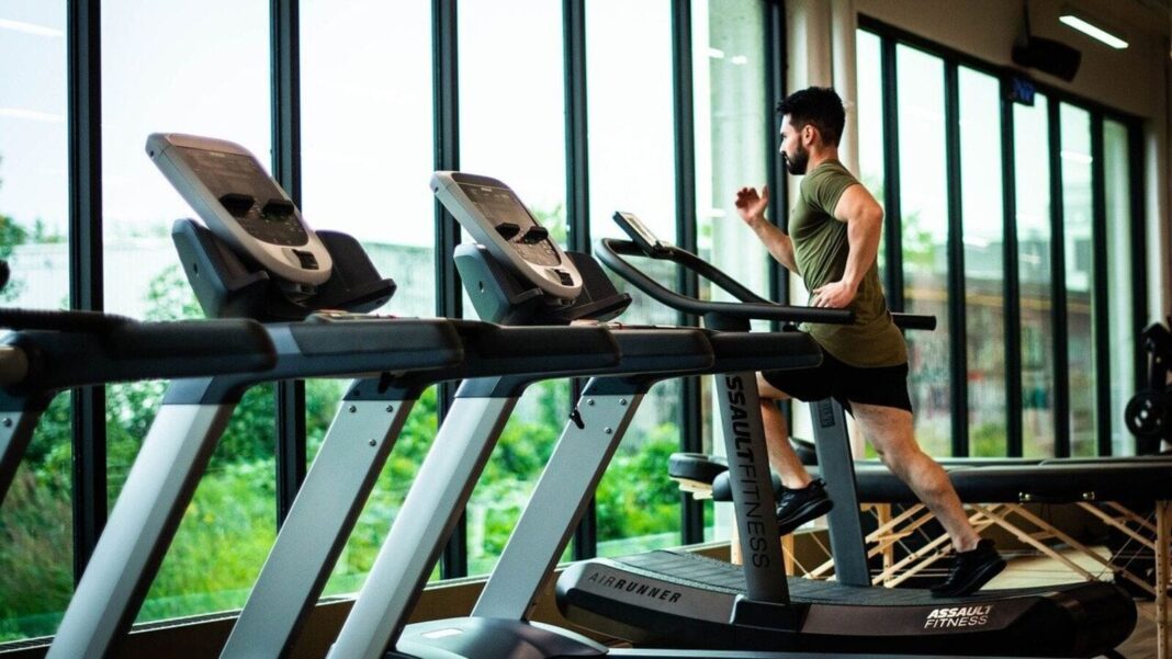 Man running on treadmill in gym with windows