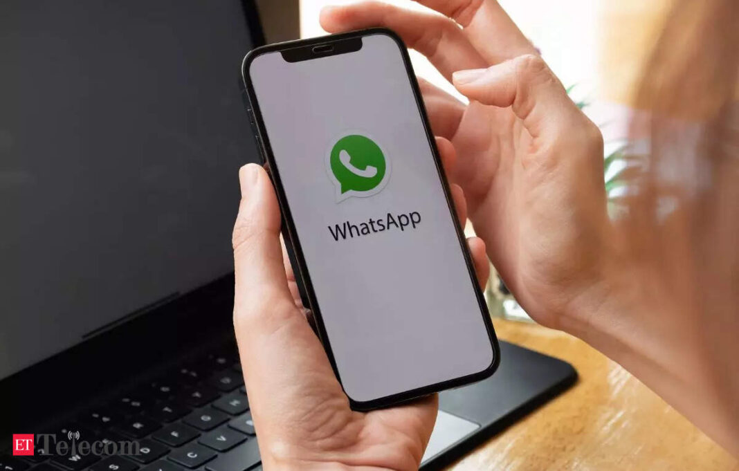 Person holding phone with WhatsApp logo on screen.