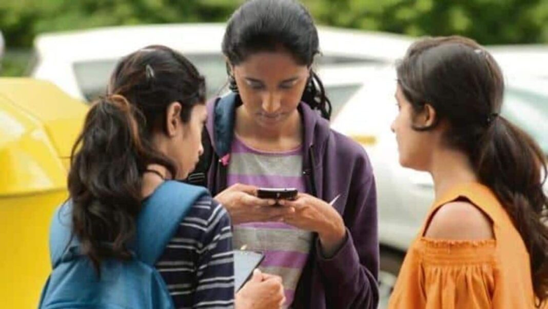 Three girls looking at smartphone outdoors.