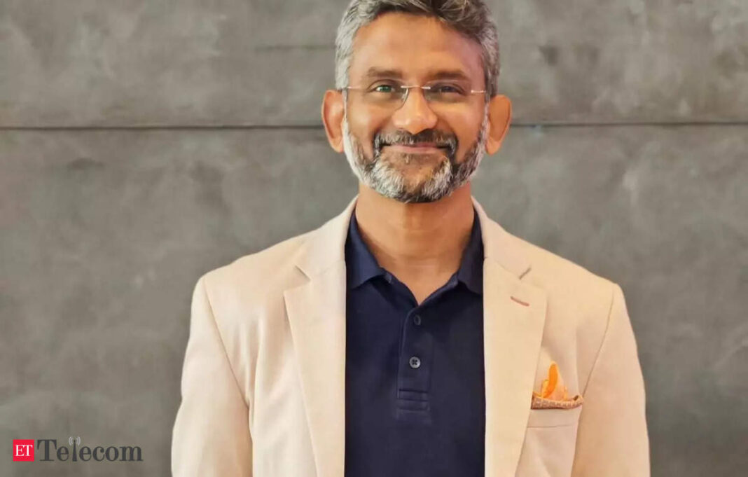 Smiling man in beige blazer with glasses.