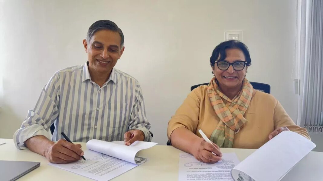 Two smiling people signing documents at office desk.