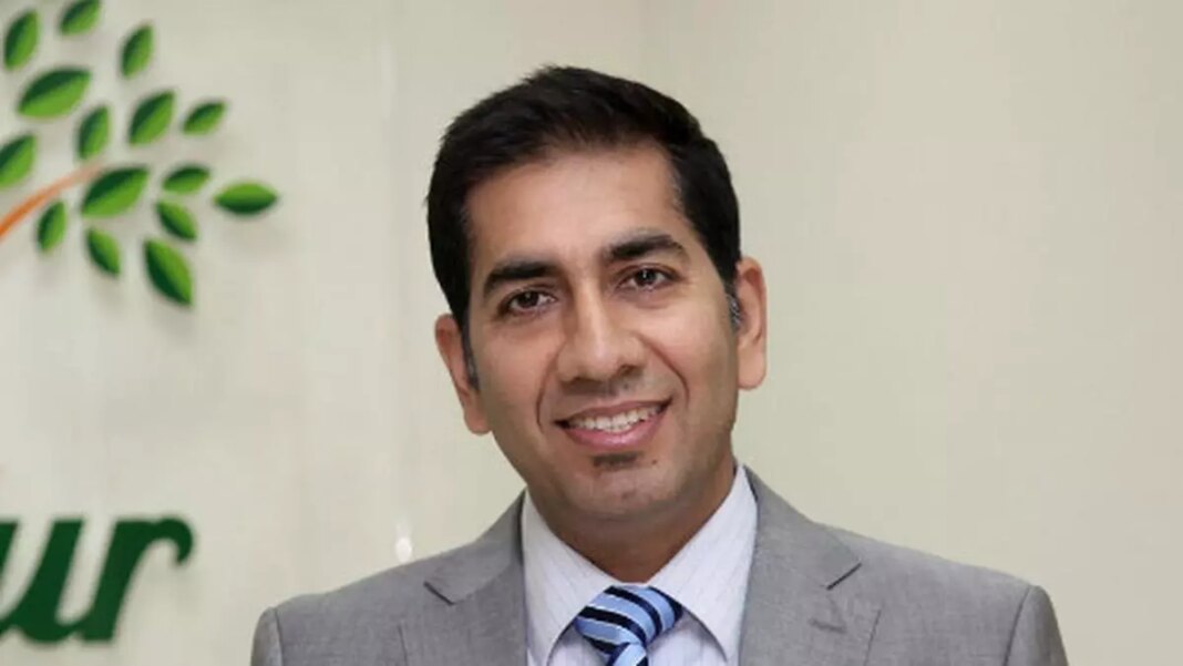 Smiling man in suit with company logo in background.