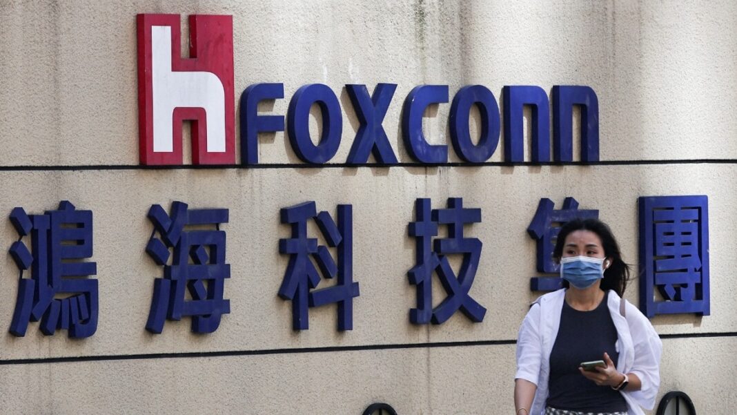 Person walking by Foxconn company sign with mask.