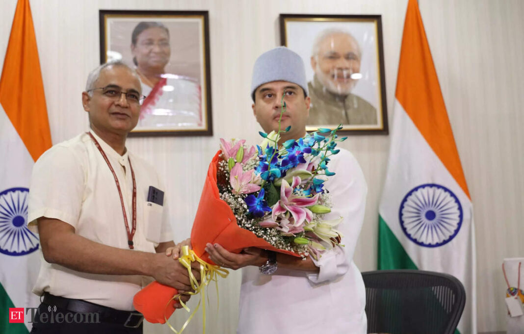 Two men exchanging bouquet with Indian flags in background.