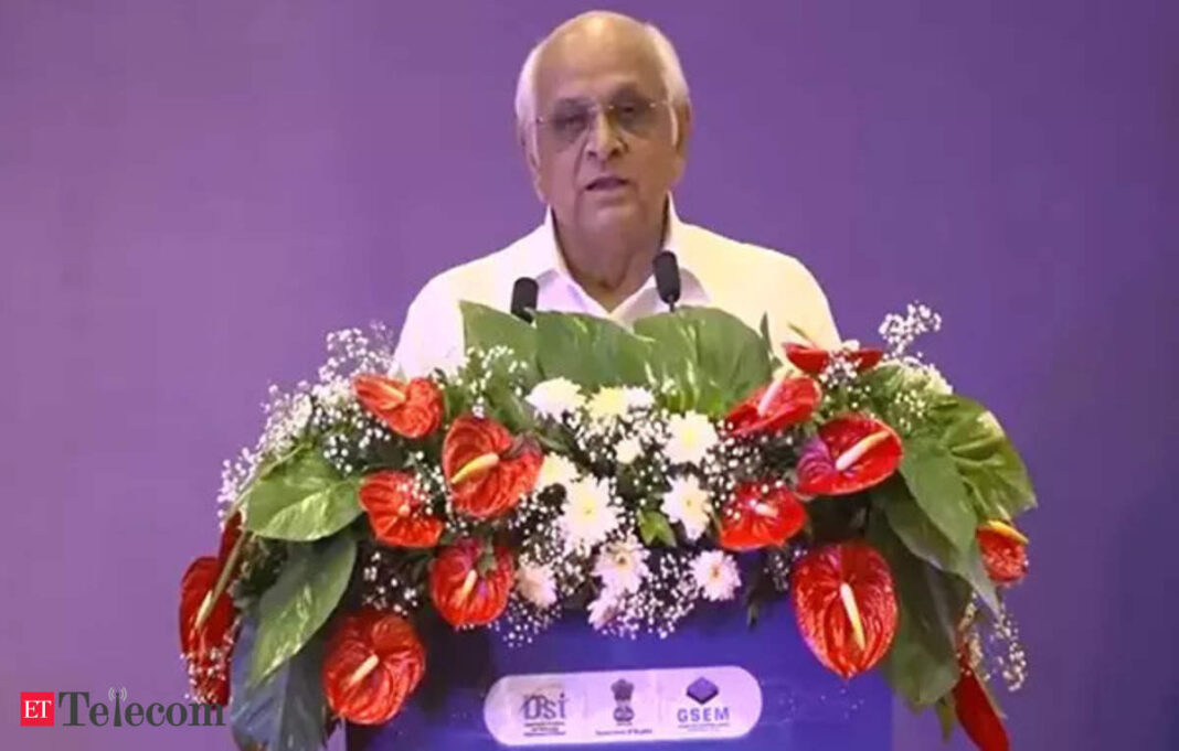 Man speaking at podium with floral arrangement.