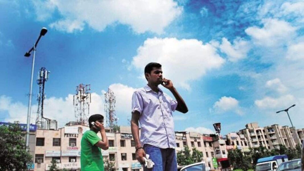 Two men using cellphones outdoors near buildings and antennas.