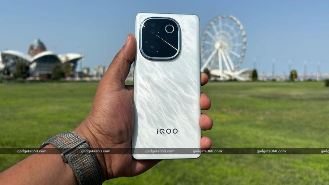 Hand holding iQOO smartphone with camera detail outdoors.