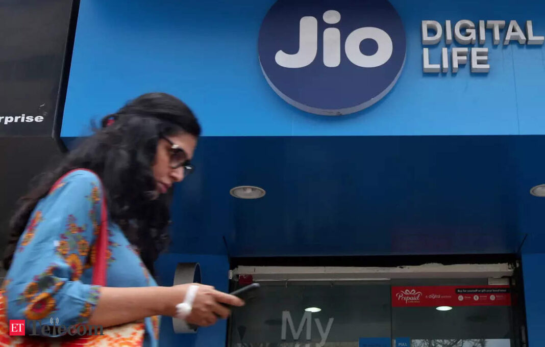 Woman walking by Jio store while using smartphone.