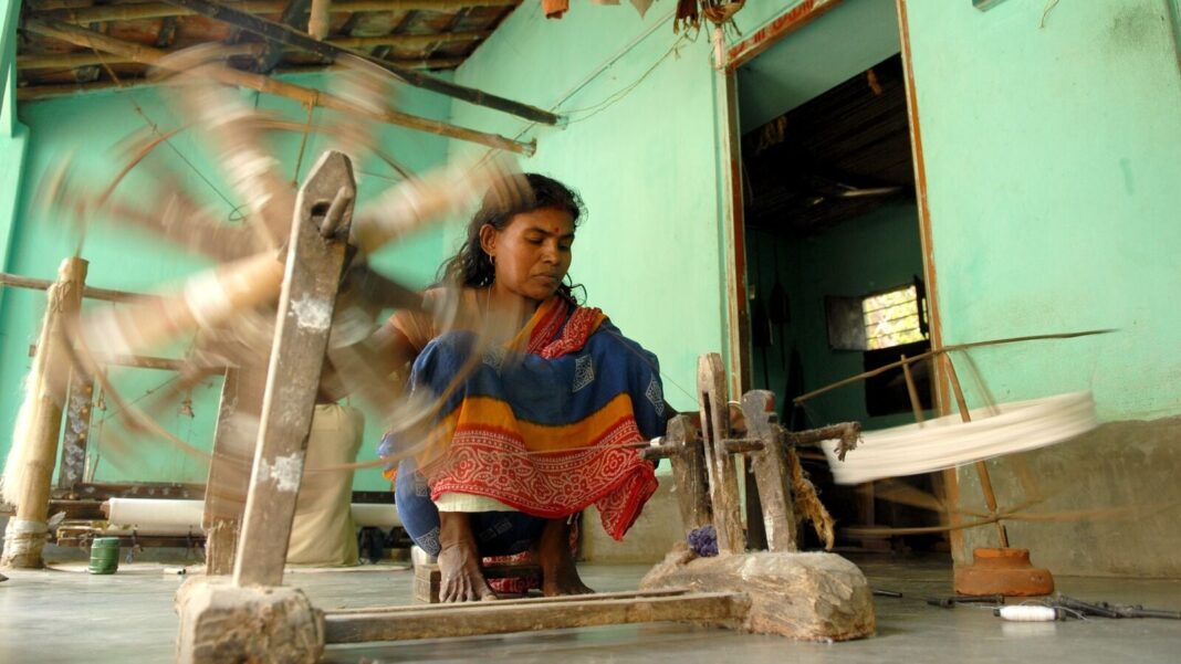 Woman operating traditional spinning wheel in workshop.