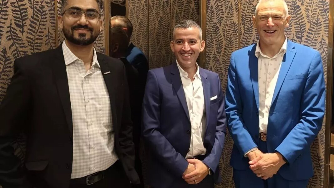 Three men posing in suits, smiling indoors.