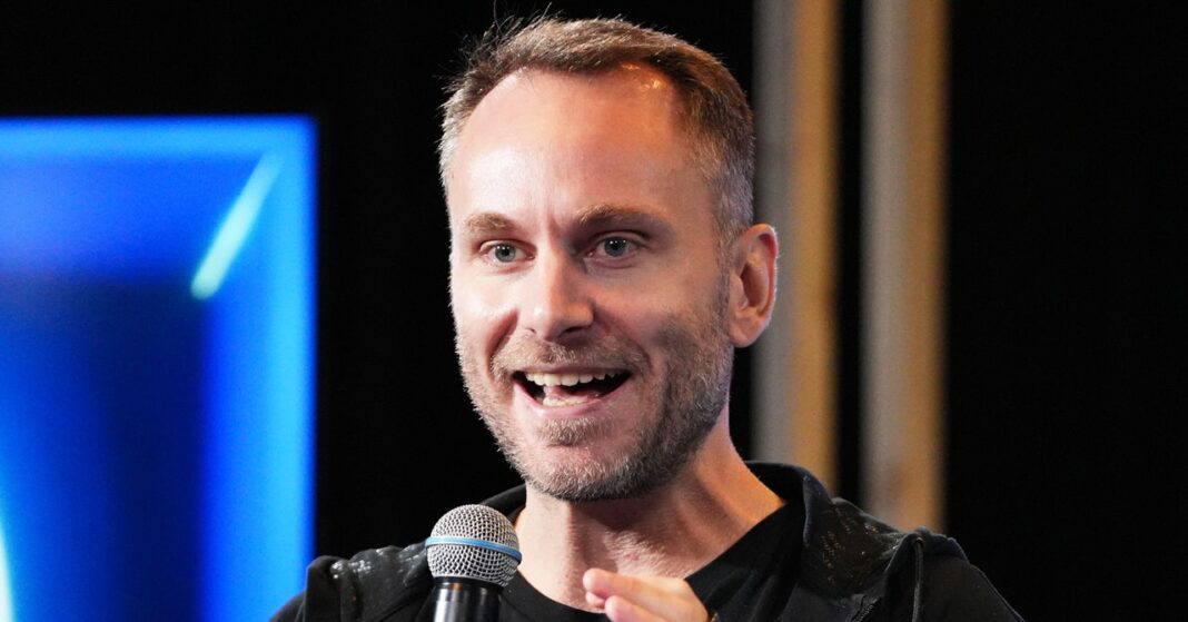 Smiling man speaking into microphone on stage.