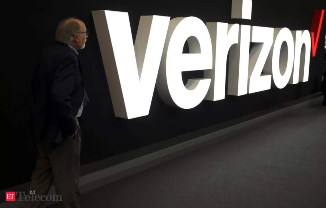 Man walking past large Verizon logo on wall.